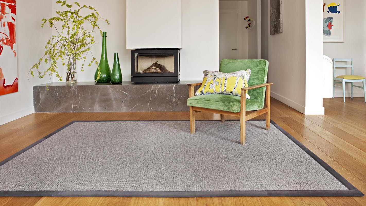 Salón con butaca de terciopelo color verde sobre alfombra de lana kansei kp alfombras a medida en color gris