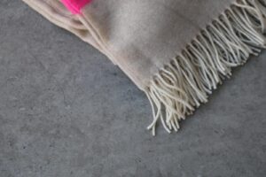 Detalle manta artesanal Maily Cecchi e Cecchi beige dos rayas fucsias en Fernández textil terminada en flecos, suave caliente