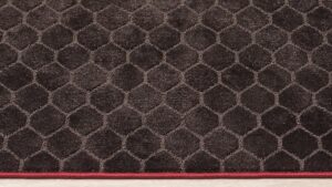 detalle diseño hexagonal en alfombra Juanola marrón modelo maya con remate rojo. Brillos en función de la luz.