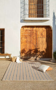 Casa bonita con alfombra en entrada exterior Rols Terra Gobi, de cuadros beige y blancos. Portón madera. Pared lisa.
