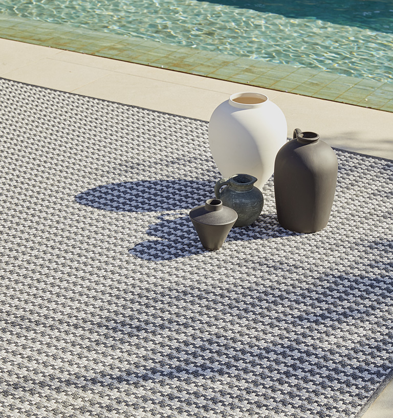 Alfombra de exterior Rols Terra Gorafe en terraza con piscina. Pata de gallo gris y blanca. Hecha en España, a medida.