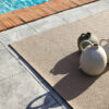 Alfombra exterior Rols Terra Sahara sobre suelo baldosa en terraza con piscina. Rústica y bonita. Duradera, diseño liso beige.
