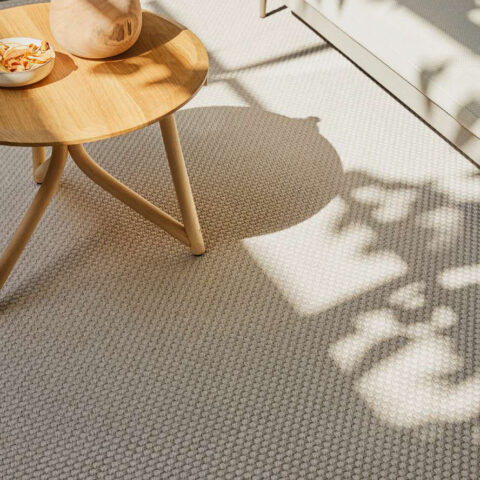 Salón exterior cubierto con alfombra Rols Terra Sahara color crudo, en tono con mobiliario y mesa de madera.
