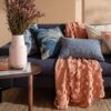 Plaid Lia Kas Australia sobre sofá oscuro, diseño pompones color salmón. Algodón 100%. Comprar online Fernández Textil