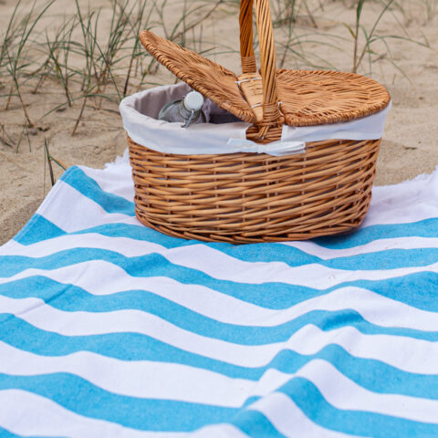 Toalla playa Bricini costa nova azul rayas blancas posada sobre arena cesto mimbre
