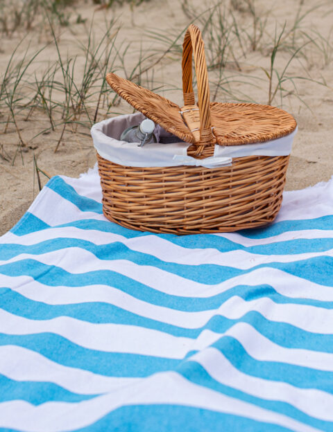 Toalla playa Bricini costa nova azul rayas blancas posada sobre arena cesto mimbre